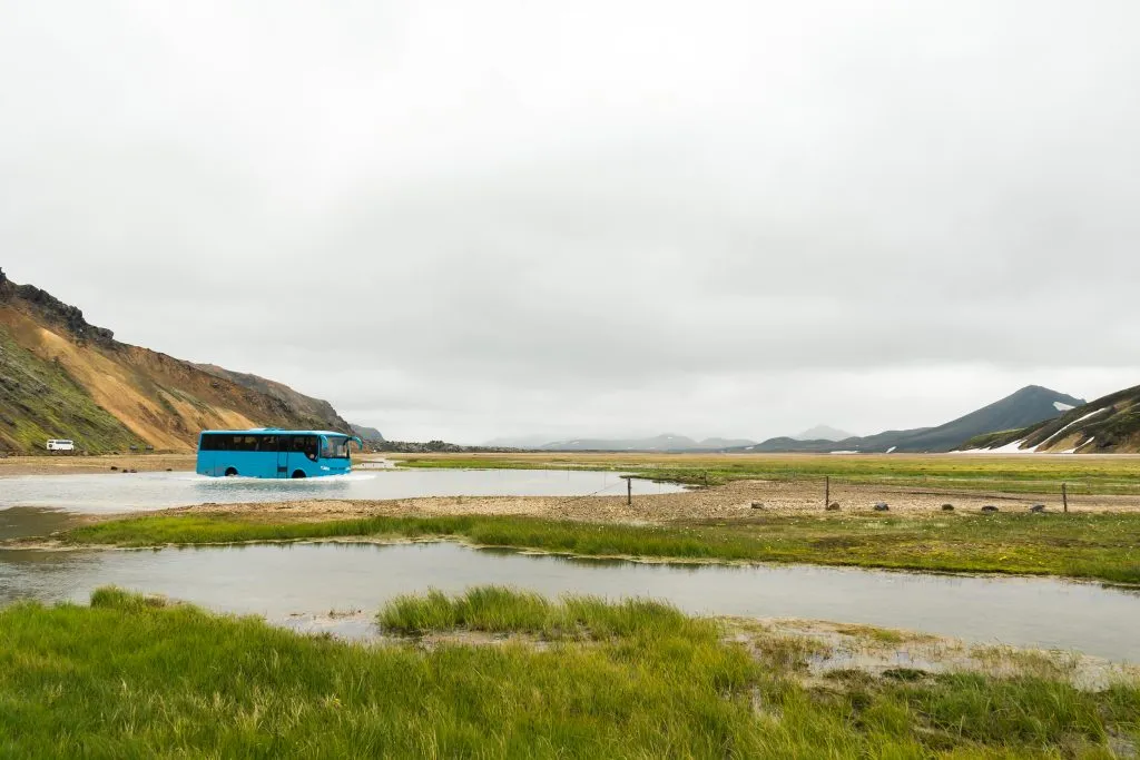 Bus crossing a river with hikers and adventurers in Landmannalaugar on a cloudy day