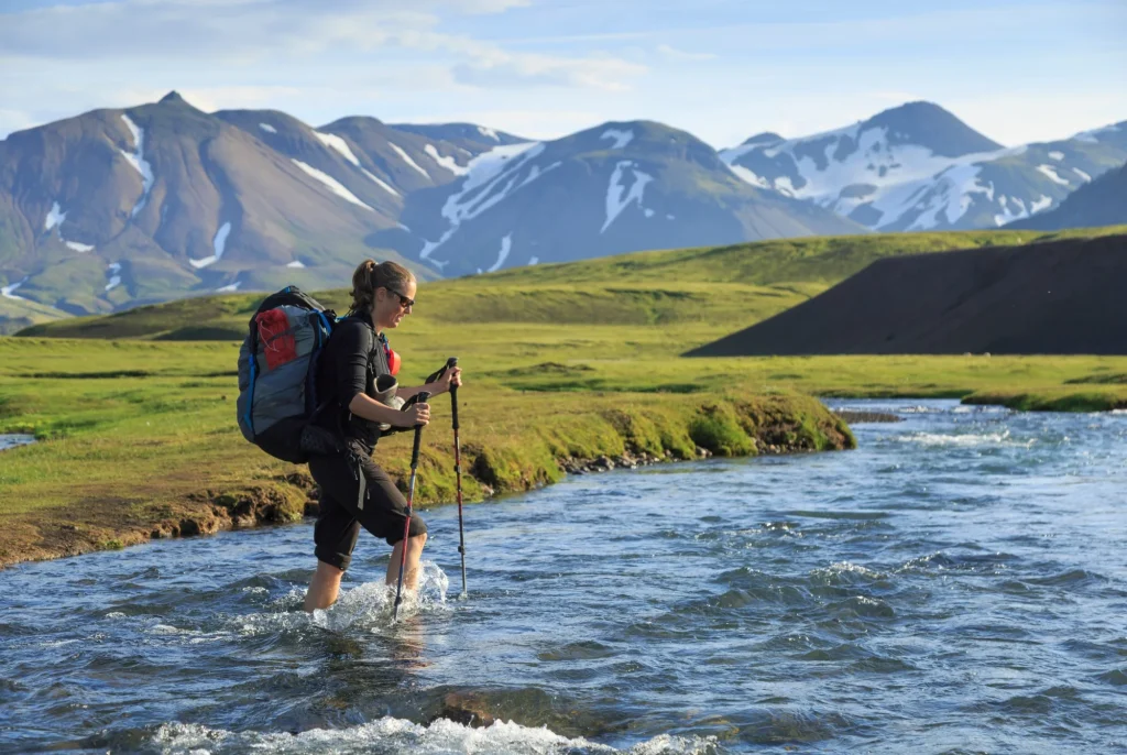 Kvindelig vandrer krydser en flod på Laugavegur-stien på Island.