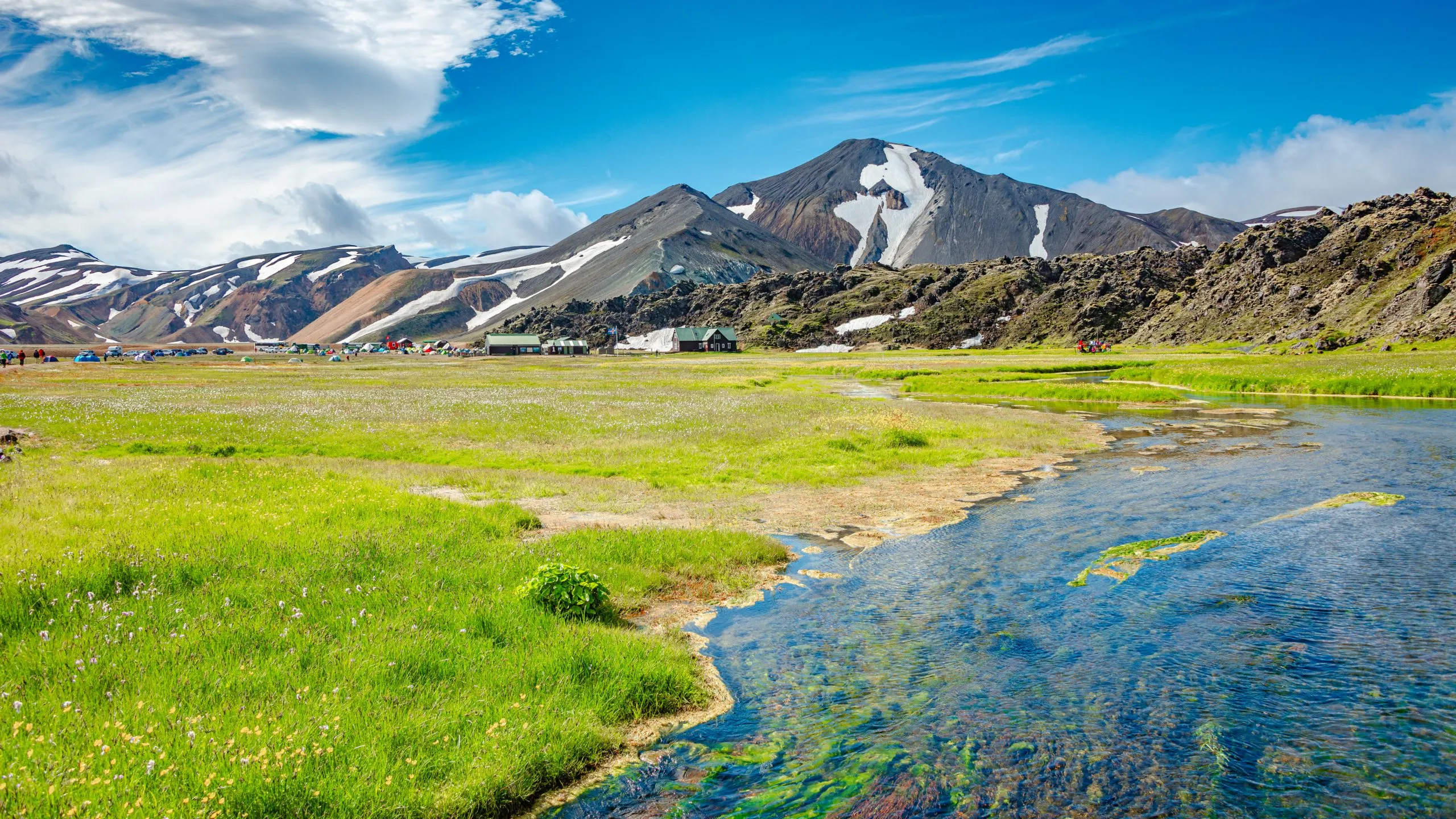 Landmannalaugar, Iceland. View at camping site and mountain hut with many tents and cars, and huge lava field, Icelandic landscape of colorful rainbow volcanic mountains at Laugavegur hiking trail